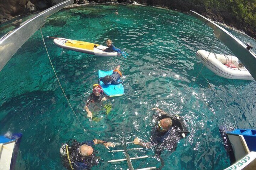 A group of people in a clear blue pool with inflatable boats and a ladder. 1