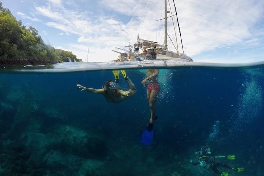 Two people snorkeling underwater with a sailboat in the background. 1