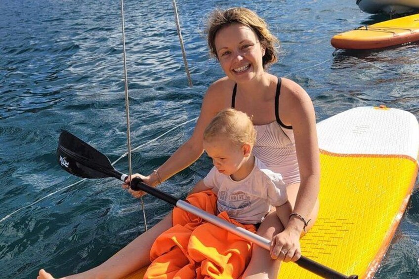 A person in a boat with a paddle, another person in a swimsuit, and a yellow paddleboard in the water. 2