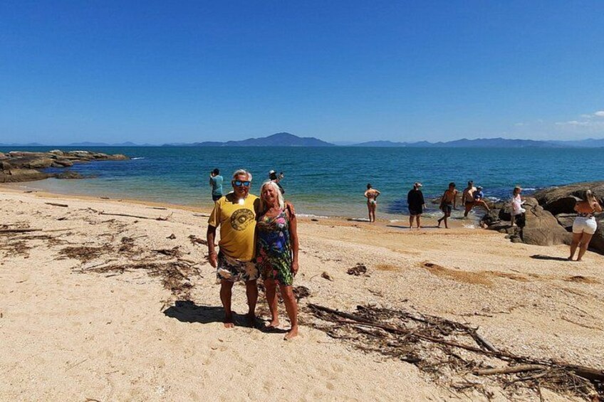 A beach with people walking and standing, rocky shoreline, and clear blue water. 5
