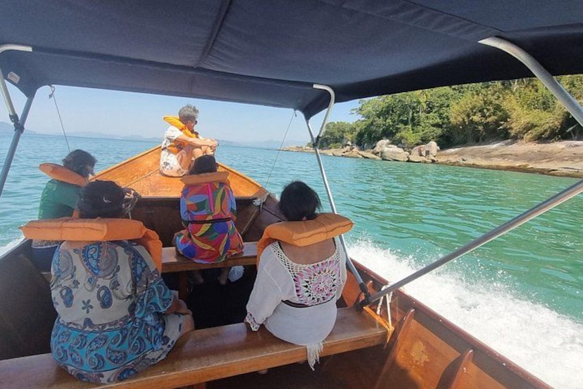 A boat with passengers wearing life jackets, moving on a body of water with a rocky shoreline in the background. 2