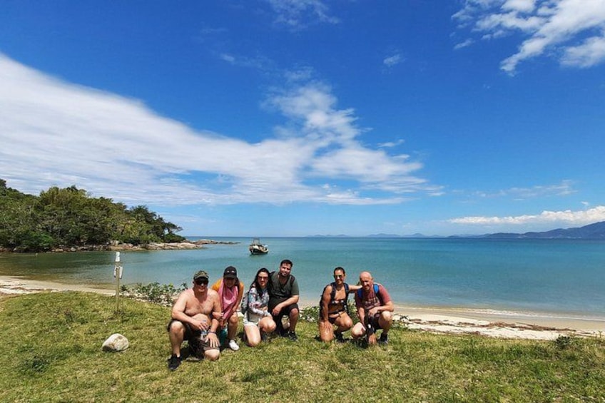 A group of people sitting on grass by a beach with a clear sky and calm sea. 4