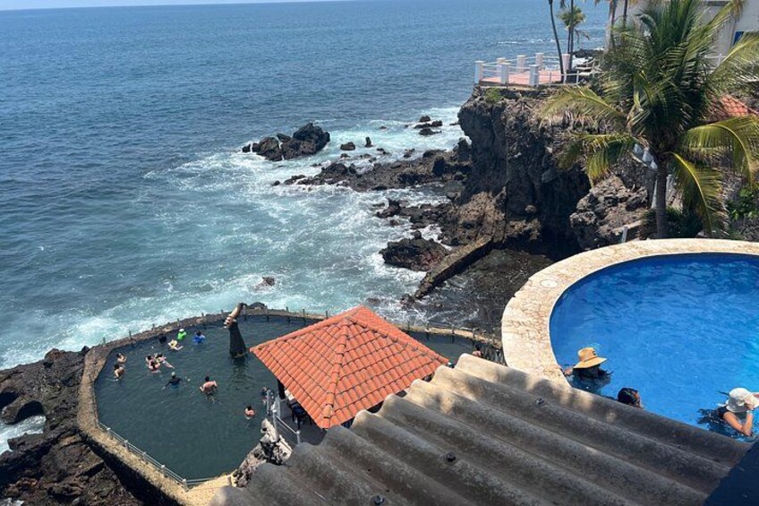 A coastal swimming area with a pool, rocky shoreline, and a red-roofed structure. 2