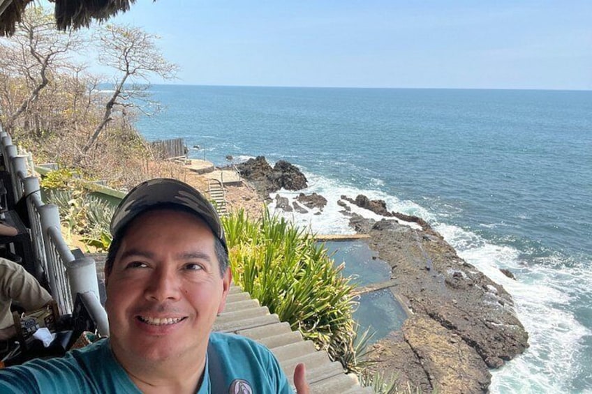 A coastal landscape with rocky shores, a clear sky, and a person taking a selfie. 2