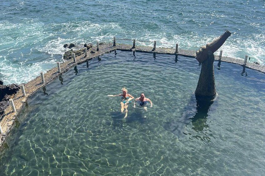 A circular pool with clear water, surrounded by a stone wall and a large rock formation. 4