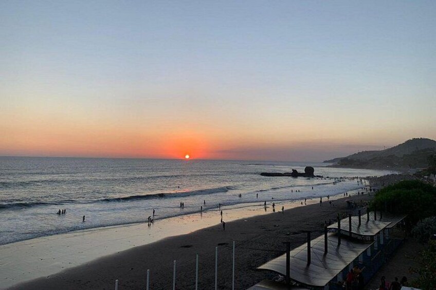 A beach at sunset with people walking and a pier extending into the water. 1