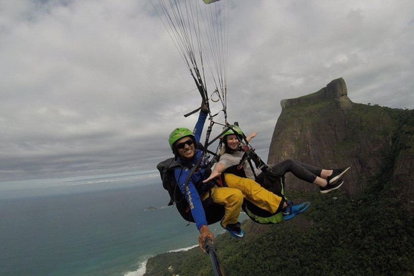 Two people paragliding over a cliff with a view of the ocean and a large rock formation. 5