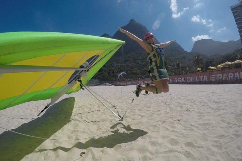 A person in a harness attached to a wing, preparing for a paragliding activity on a beach with mountains in the background. 3