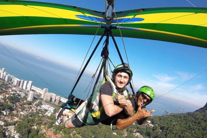 A person in a harness attached to a winged apparatus, with a cityscape and coastline in the background. 2