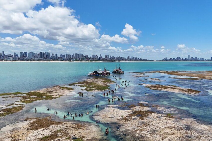 A coastal cityscape with a clear sky, a beach with people, and boats. 1