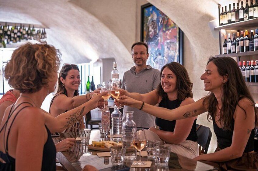 Un grupo de personas brindando con copas de vino en un bar con pared de piedra y estantes llenos de botellas. 1
