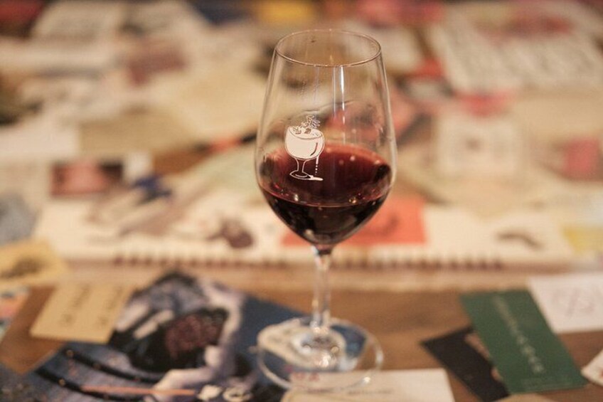 Una copa de vino con líquido rojo sobre una mesa con diversos papeles y tarjetas. 4