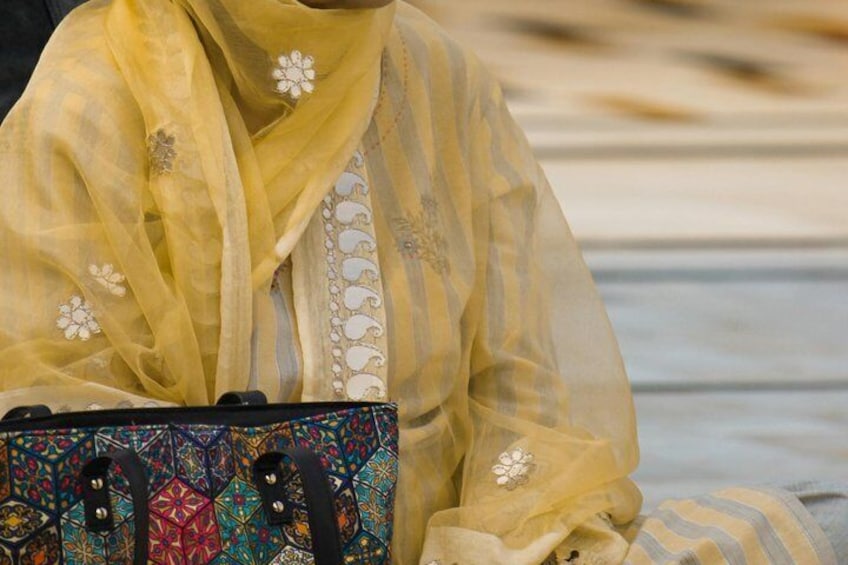 A person in a yellow patterned outfit holding a colorful bag with intricate designs. 5