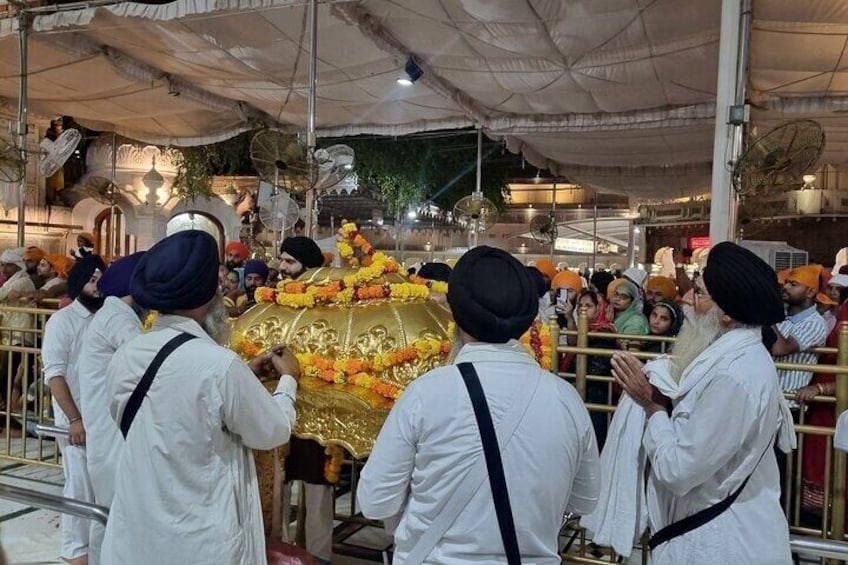 A group of people in white robes and turbans gathered around a golden structure adorned with flowers. 4