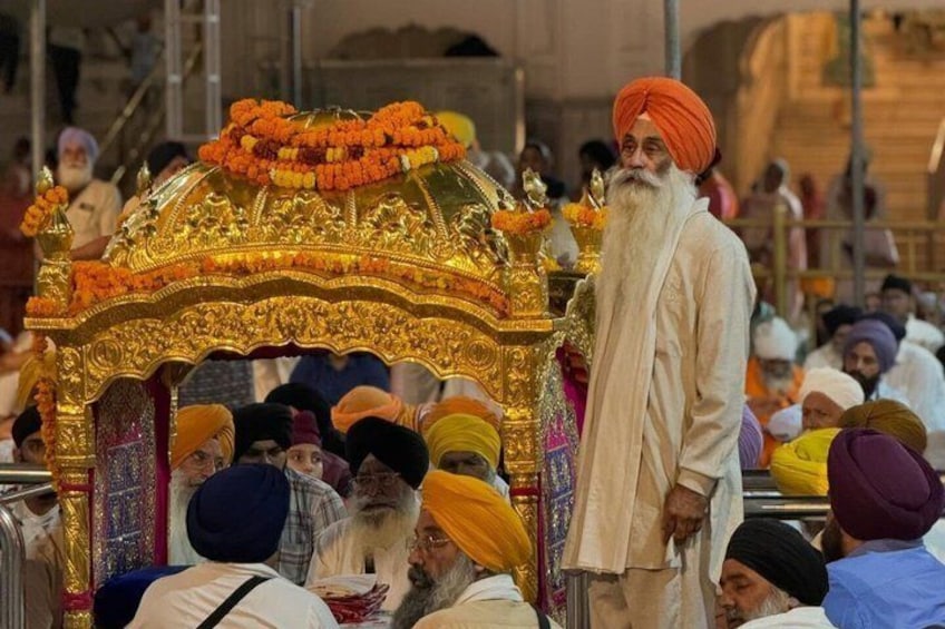A group of people in traditional attire, a golden ornate structure, and a person standing in front of it. 1