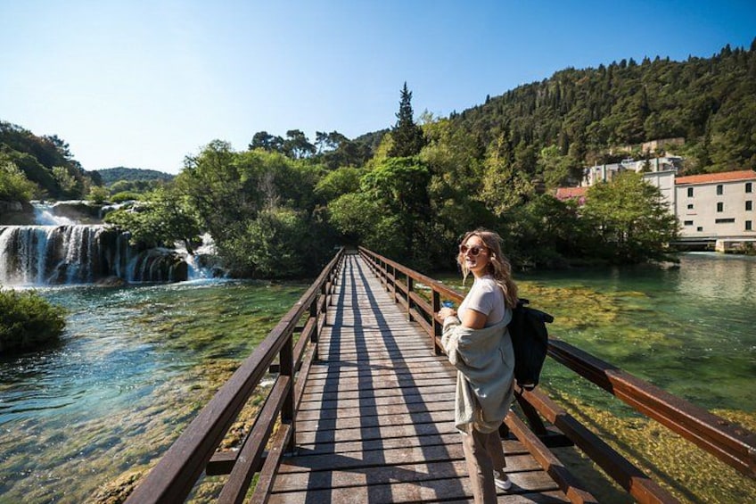 A wooden bridge over a river with a waterfall in the background. 1