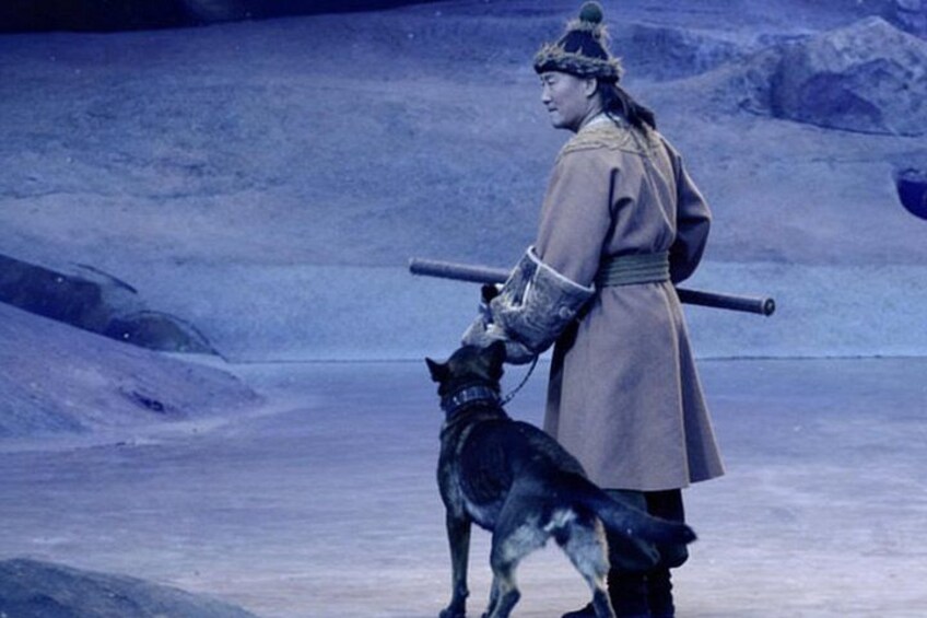 Une personne vêtue d’un costume traditionnel, tenant un bâton, se tient dans un paysage enneigé, accompagnée d’un chien. 4