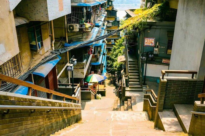 A narrow urban stairway with multiple levels of buildings, a person with a colorful umbrella, and a visible staircase on the right. 5