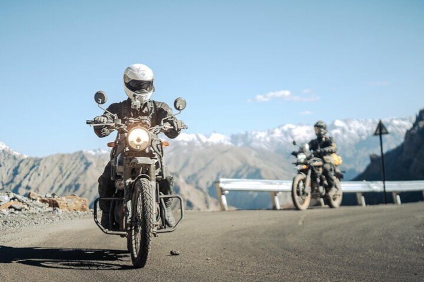 Two motorcyclists on a road with mountains in the background. 4