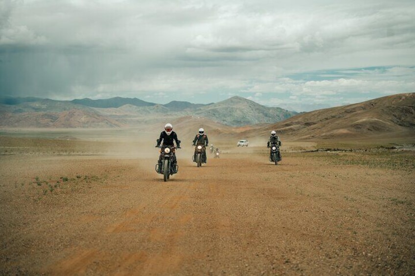 Three motorcyclists riding on a dirt road with a mountainous landscape in the background. 3