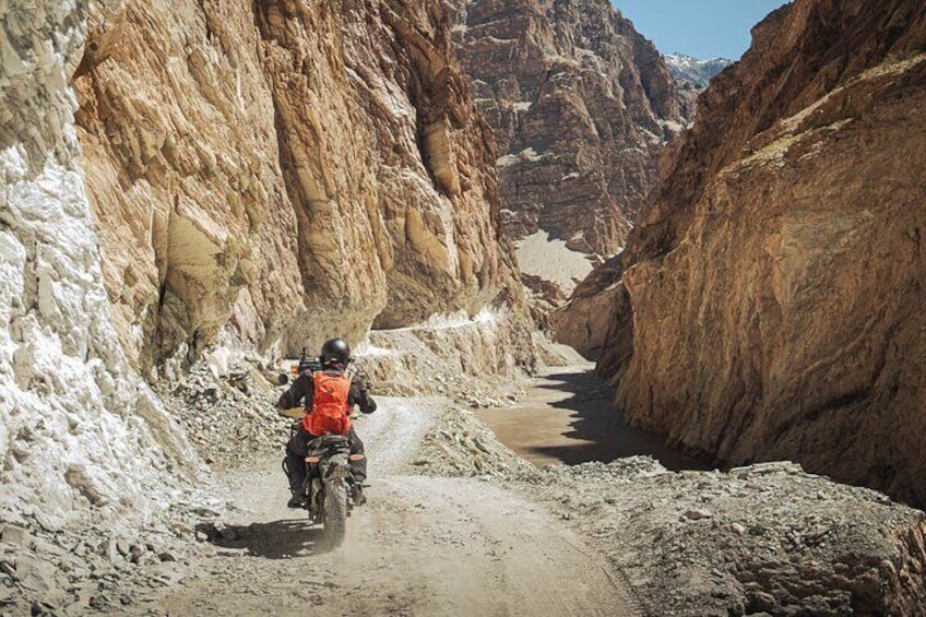 A person riding a motorcycle through a narrow canyon with rocky walls. 5