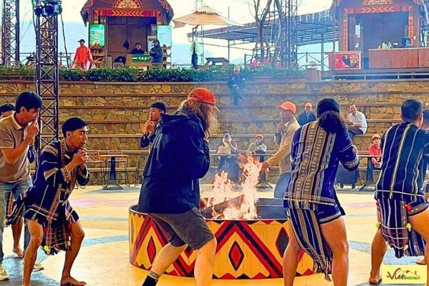 A group of people performing a fire dance in an outdoor setting with a stage and audience in the background. 1