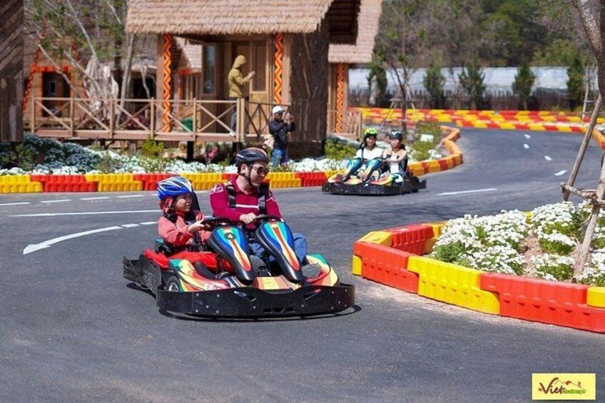 Personas en karts sobre una pista, con un edificio de techo de paja al fondo. 5