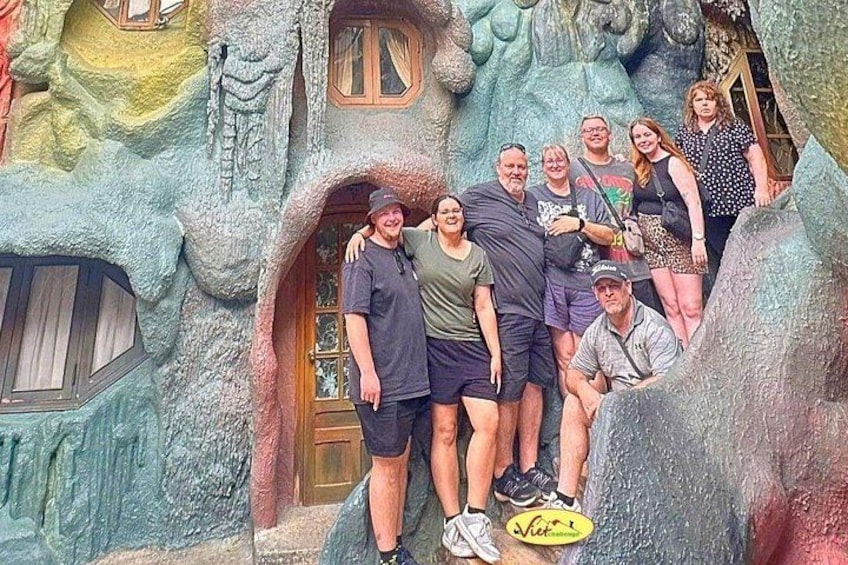A group of people posing in front of a whimsical, textured building with a door and windows. 2