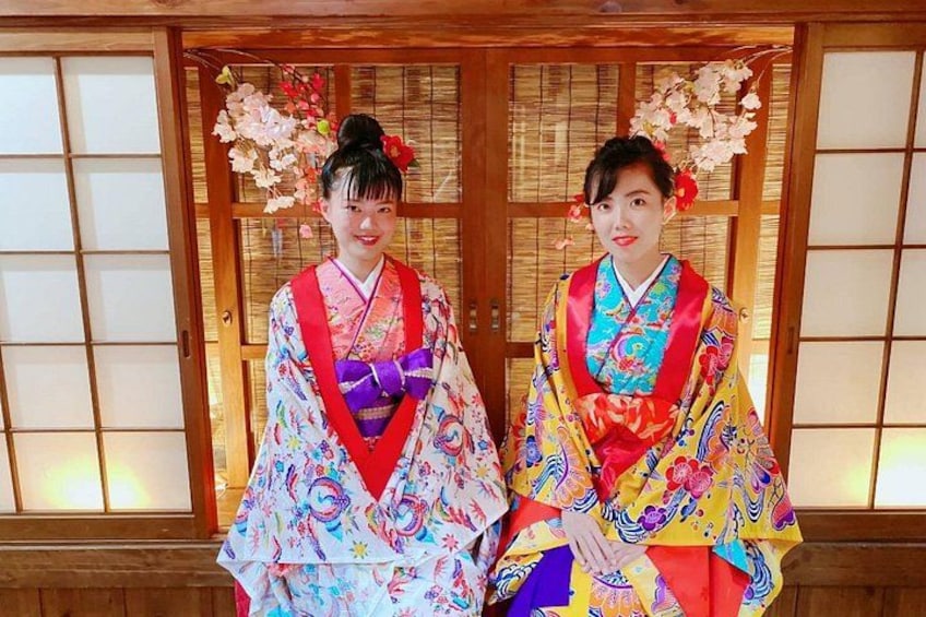 Two individuals in colorful kimonos with floral decorations, standing in front of a traditional wooden door with glass panels. 3