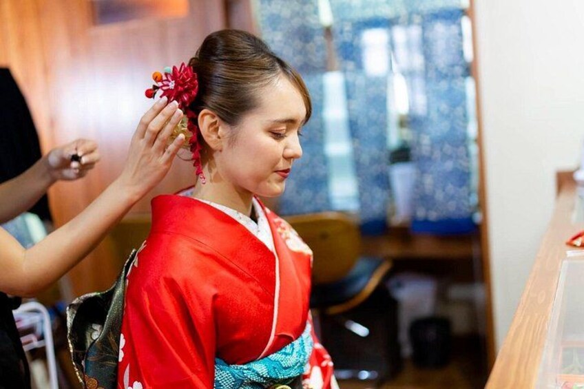 A person in traditional attire with a red and blue garment, seated indoors. 1