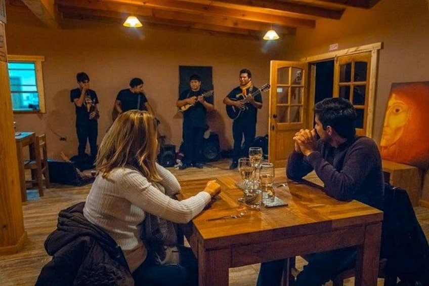 Un interior de madera con una banda tocando, una mesa de comedor con vasos, y un cuadro en la pared. 2