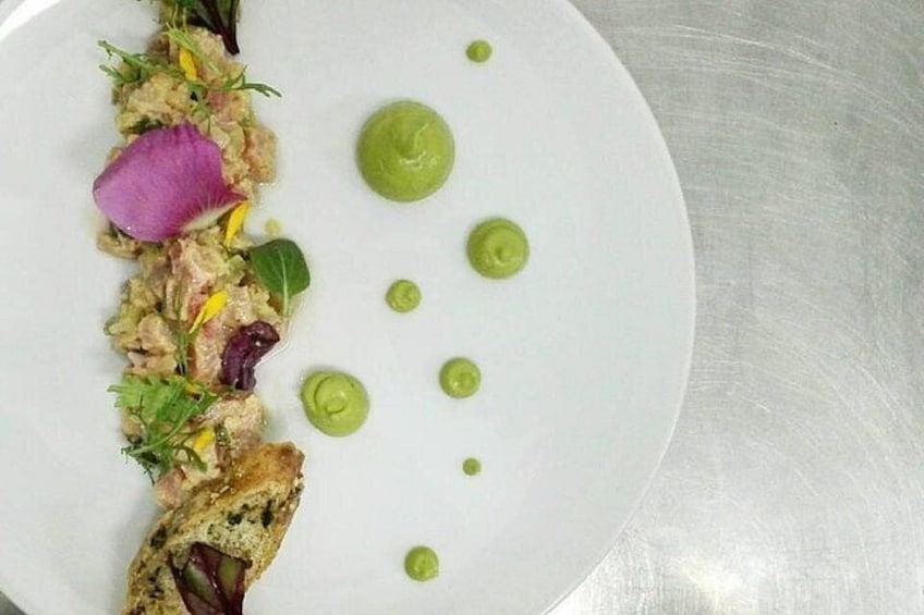 Un plato blanco con una presentación de alimentos, que incluye vegetales, una flor rosa y un trozo de carne. 5