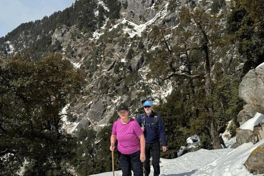 Twee mensen wandelen over een met sneeuw bedekt pad, met rotsachtige bergen op de achtergrond. 2