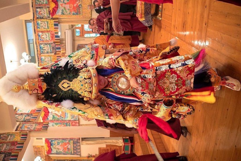 A person in traditional colorful attire with intricate patterns and decorations, standing in a room with wooden flooring and various artworks on the walls. 4