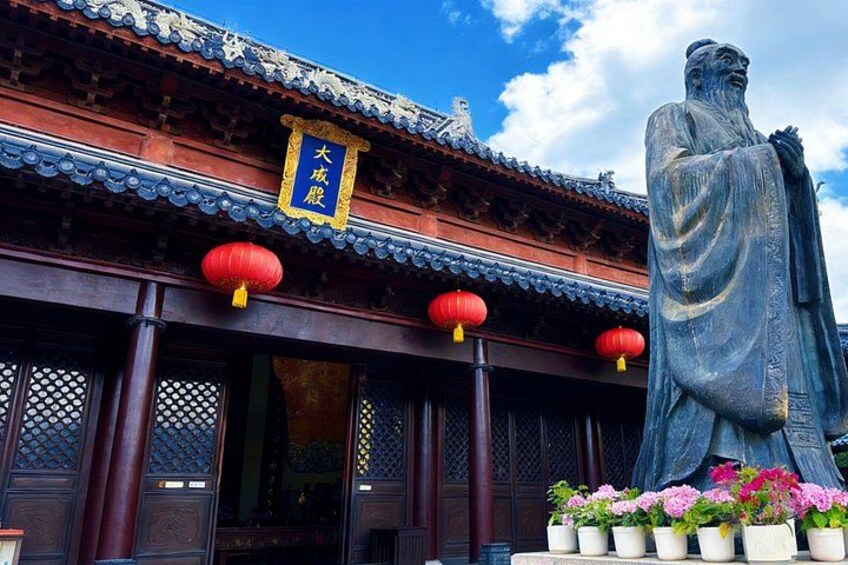 A traditional Chinese building with a large statue, red lanterns, and potted flowers. 2