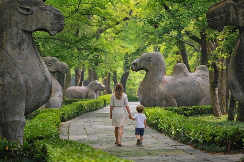 A pathway lined with large stone animal sculptures, a woman and child walking, and lush greenery. 1