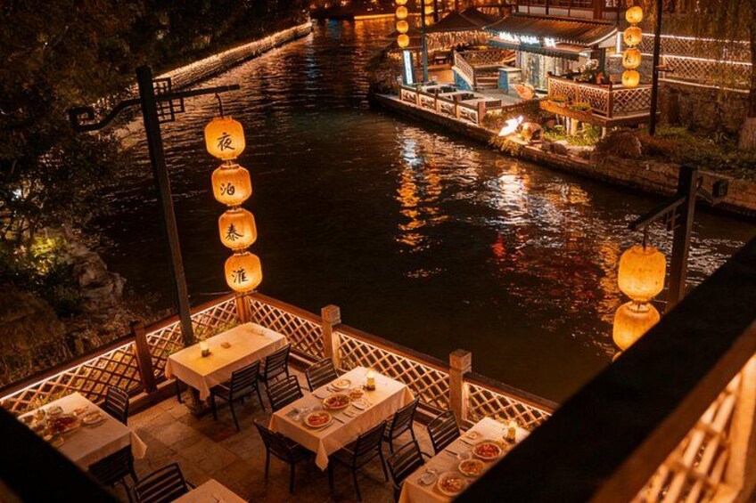 A riverside restaurant with tables and chairs, illuminated by hanging lanterns. 3
