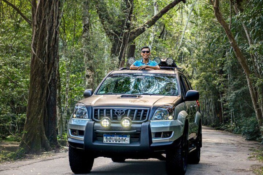 A brown SUV on a forest road with a person in the driver's seat. 1