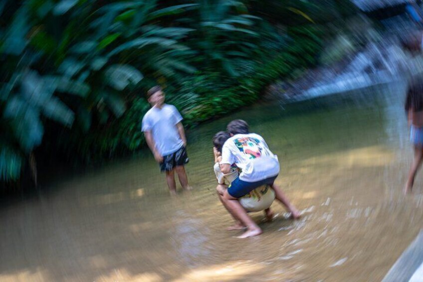 A person playing rugby in a muddy field with dense foliage in the background. 3