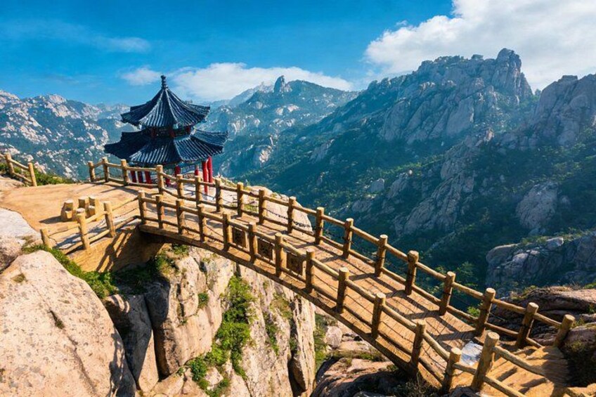 A wooden bridge with a pagoda, rocky terrain, and mountains in the background. 1