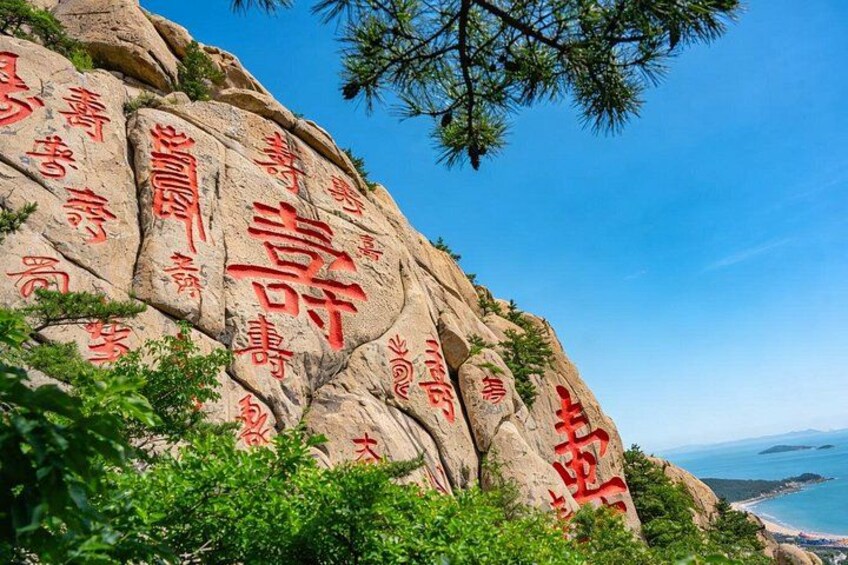 A rock face with carved red Chinese characters, surrounded by greenery and overlooking a coastal landscape. 4
