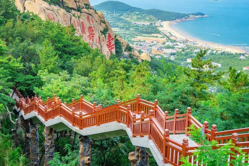 A staircase with red railings leading up a mountain, overlooking a coastal town and beach. 3