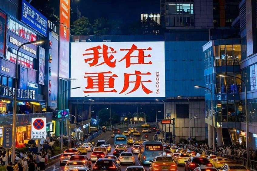 A busy urban street at night with a large illuminated billboard in the center. 4