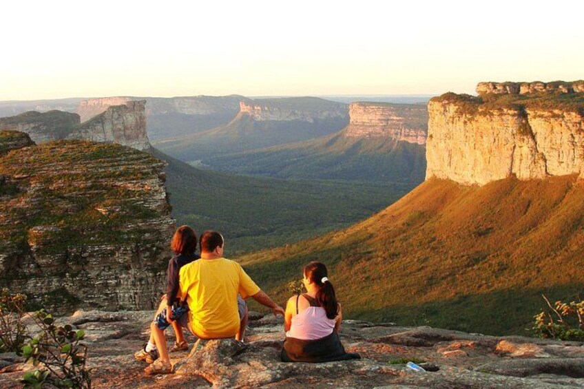 Un grupo de personas sentado sobre un afloramiento rocoso con vistas a un cañón con acantilados pronunciados y un valle. 2