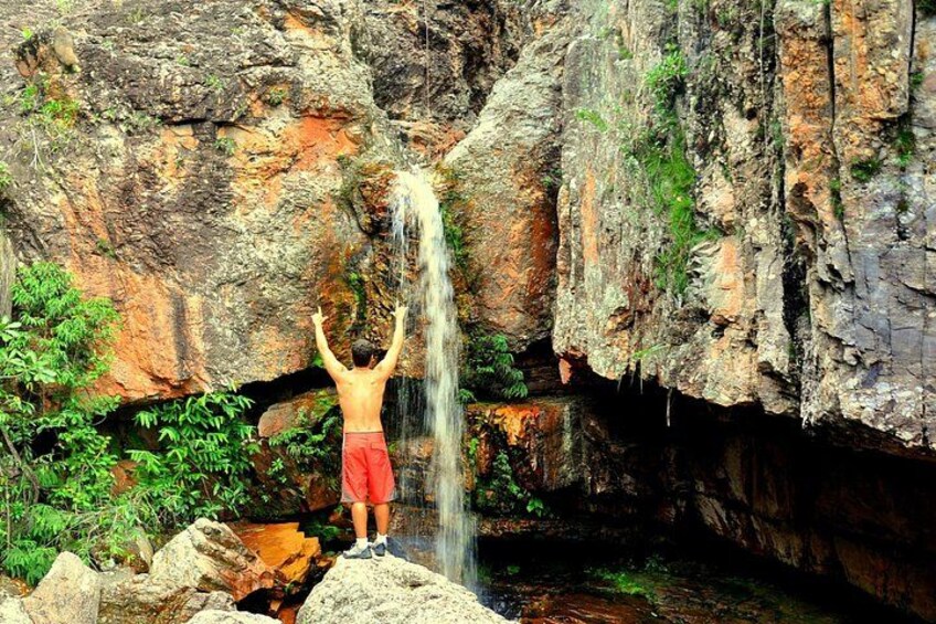 Una persona de pie sobre rocas con los brazos levantados, mirando un cascada. 4