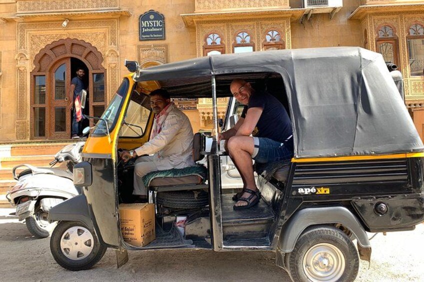 An auto-rickshaw parked in front of a building with ornate architecture. 1