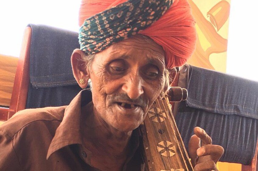 An elderly person playing a stringed instrument, wearing a turban. 2
