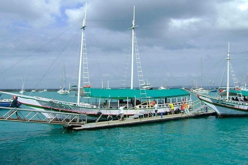 Un puerto con varios barcos de vela tradicionales amarrados, un edificio con techo verde y aguas turquesas tranquilas. 2