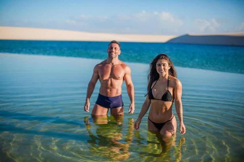 Två personer står i grunt vatten med fri sikt över havet och en avlägsen landmassa. 1