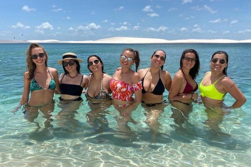 En grupp människor i klart vatten, med en sandstrand och en klar himmel i bakgrunden. 4